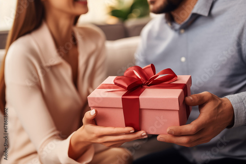 Close-up, husband surprises wife with gift, Valentine's Day, living room sofa, focus on present.
