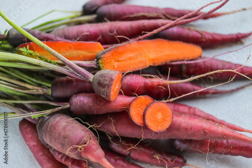 Organic carrot harvest with bright orange hue core and purple peel close-up on grey table