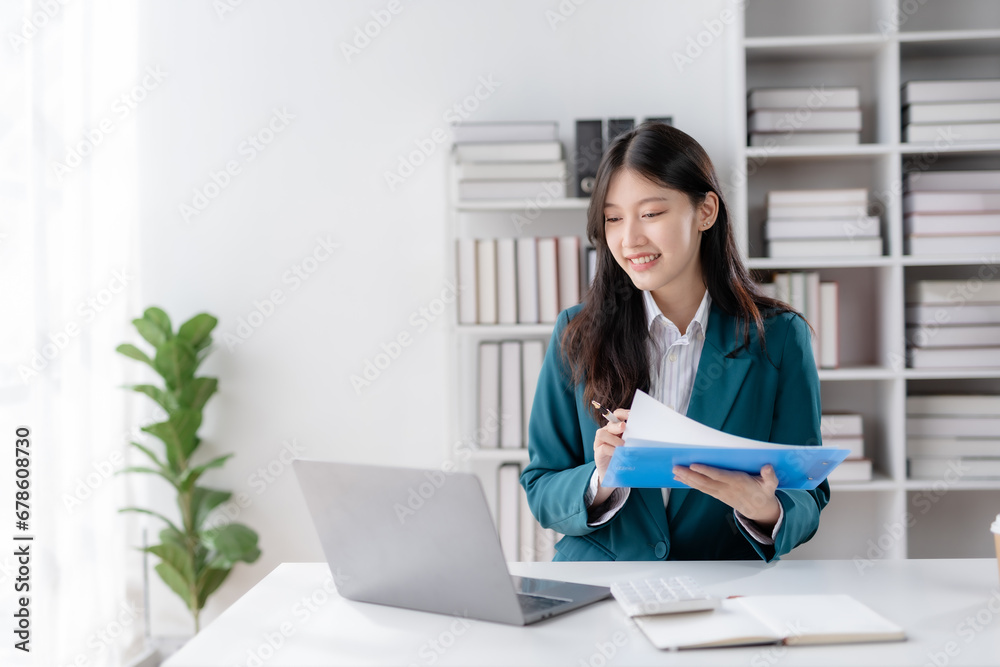 Financier working with documents at workplace. Young Asian business woman sitting working in modern office with documents and laptop computer. Financier working with documents at workplace. Young Asian business woman sitting working in modern office with documents and laptop computer.