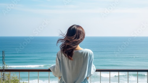 The back of a woman stands on the hotel balcony, looking at the sea alone.