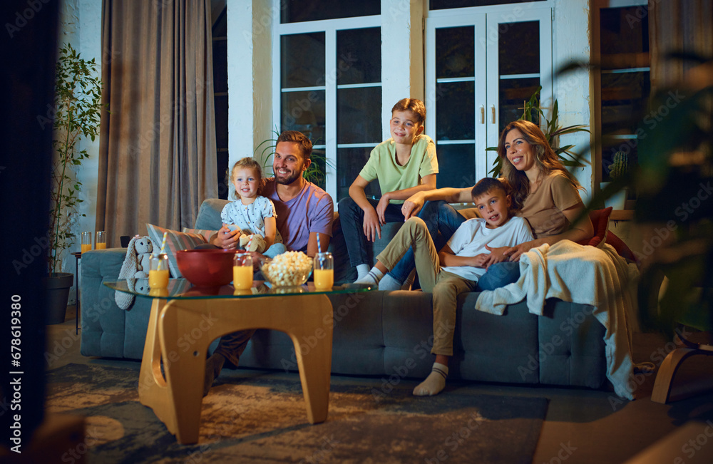 Happy smiling family, children with parents watching tv on couch in the evening. Positive emotions, cozy time together. Concept of family, leisure time, relaxation, childhood and parenthood