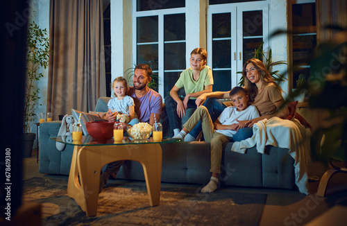 Happy smiling family, children with parents watching tv on couch in the evening. Positive emotions, cozy time together. Concept of family, leisure time, relaxation, childhood and parenthood