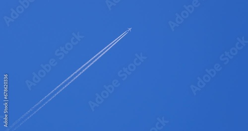 Airplane flying on deep blue sky with chemical direction trails, view from a distance