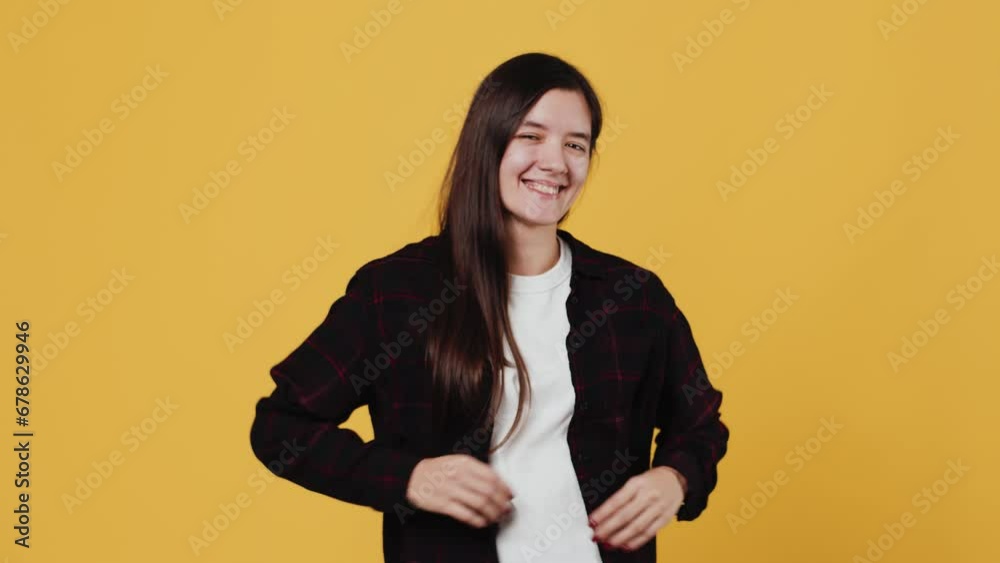 Young attractive woman smiling and laughing and looking at the camera with a contented face when puts her hands on her hips on a yellow background in the studio Young attractive woman smiling and laughing and looking at the camera with a contented face when puts her hands on her hips on a yellow background in the studio