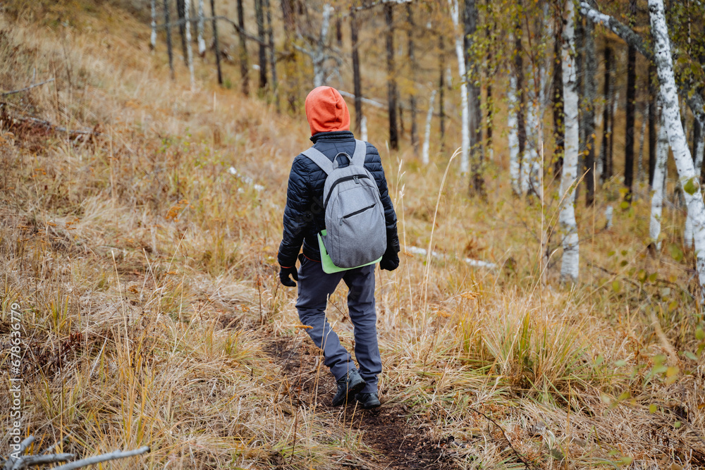 A man with a backpack on his back confidently walks along a mountain trail, a hiker on a hike moves along the azimuth, autumn hiking in a national park.