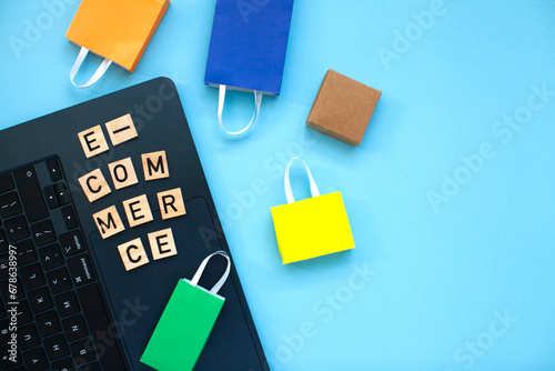 E-commerce and online shopping concept. Laptop, colourful bags and  wooden letters on the blue background. Top view.