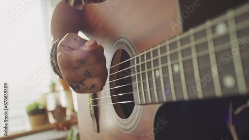 Close up of hands of unrecognizable woman using pick while playing acoustic guitar indoors photo