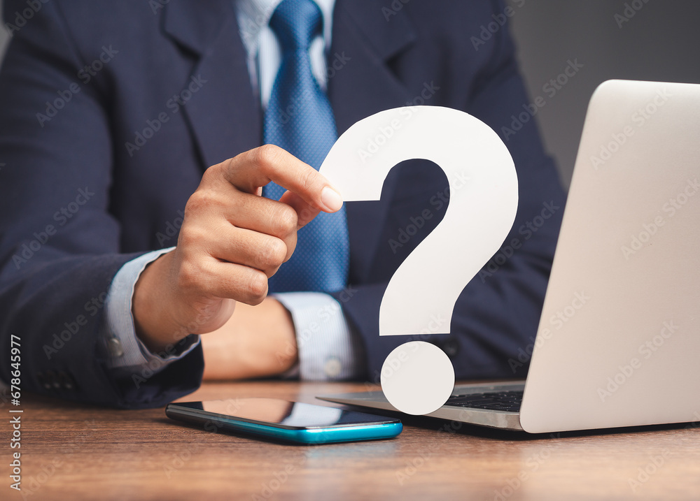 Businessman holds a white question mark symbol sitting at the table. Businessman holds a white question mark symbol sitting at the table.