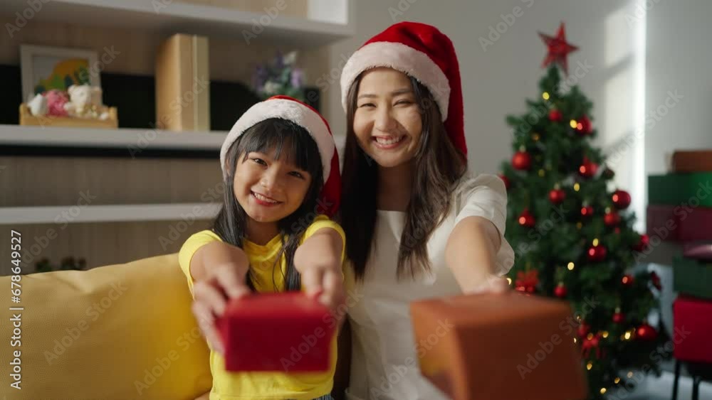 Christmas family celebration. Happy asian woman and little girl with gift in santa claus hats at home. Mother and daughter holding gifts and smiling to camera Family enjoy winter holidays
