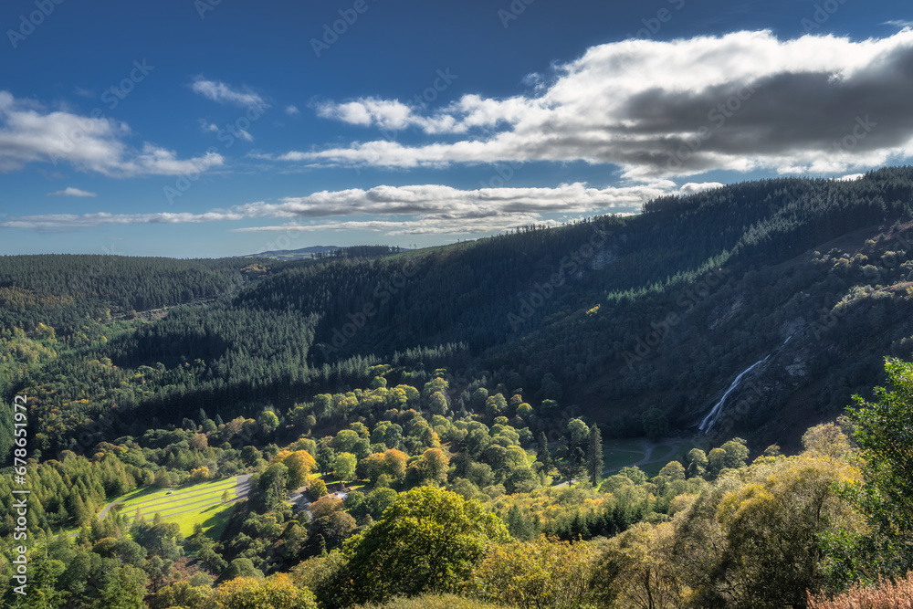 Tall Powerscourt Waterfall, valley, forests in autumn colours illuminated by sunlight. Scenic Wicklow Mountains, Ireland