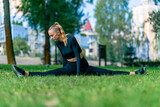 A young beautiful girl sits on the splits and does stretching after training in the morning in park