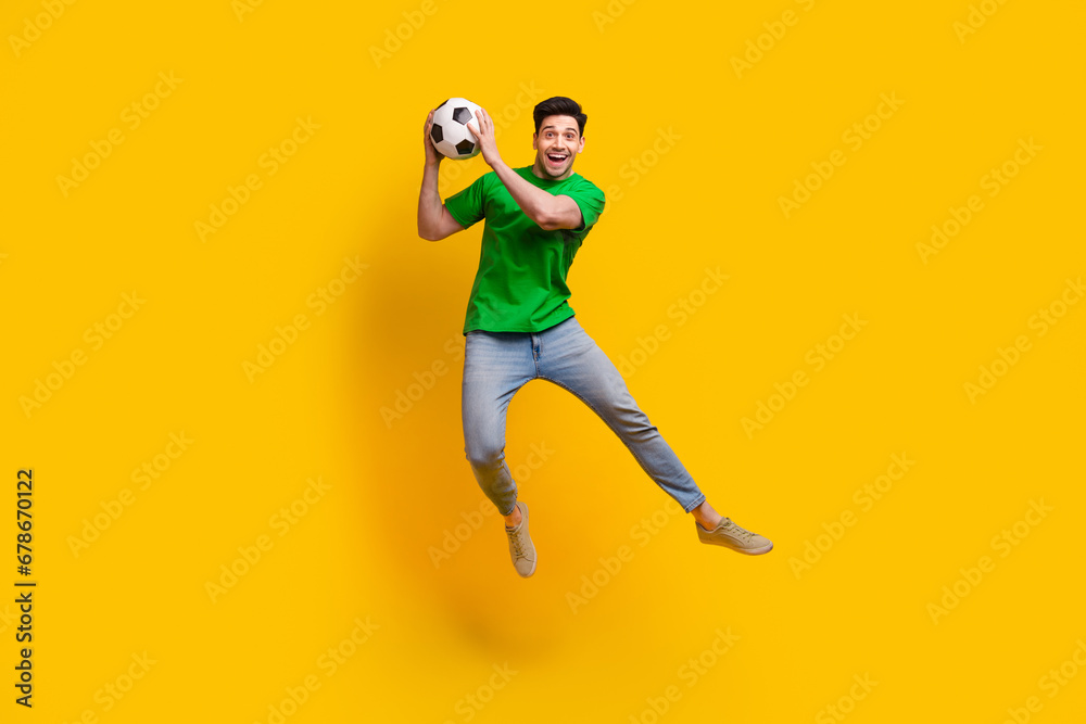 Full size photo of excited impressed goalkeeper wear stylish t-shirt jeans catching football ball isolated on yellow color background