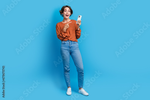 Full body photo of pretty young girl point excited gadget sales dressed stylish brown outfit isolated on blue color background
