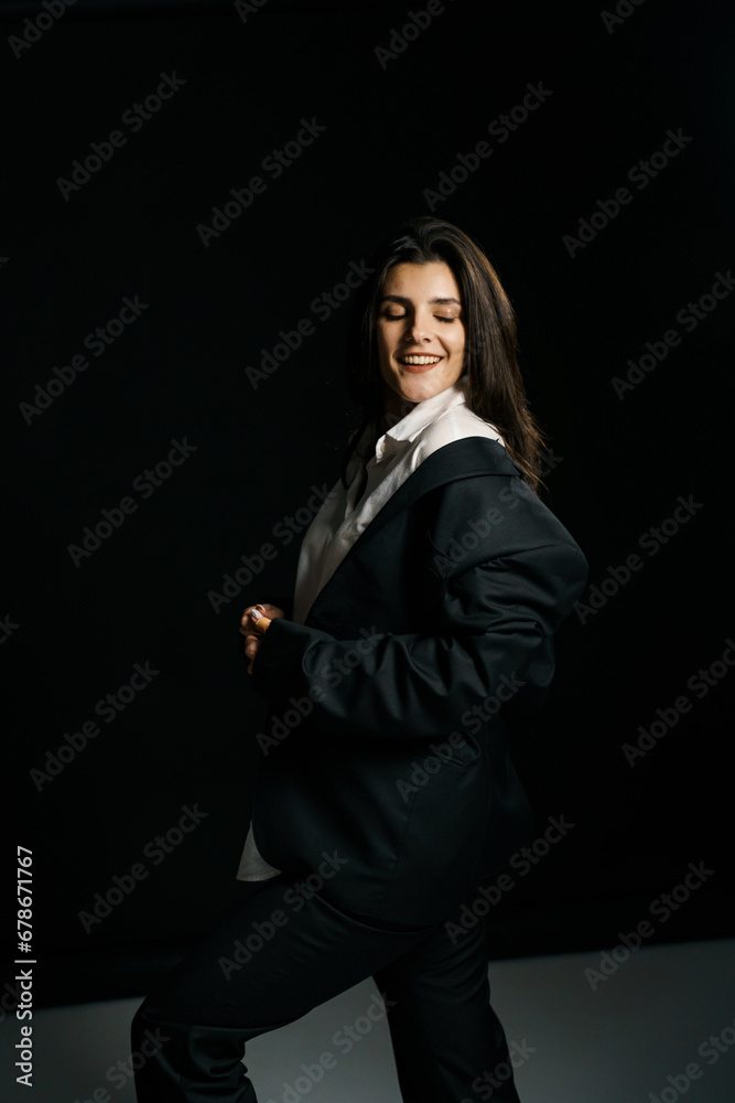 Stylish girl posing in a black suit and white shirt in a professional photo studio. Fashion shooting concept
