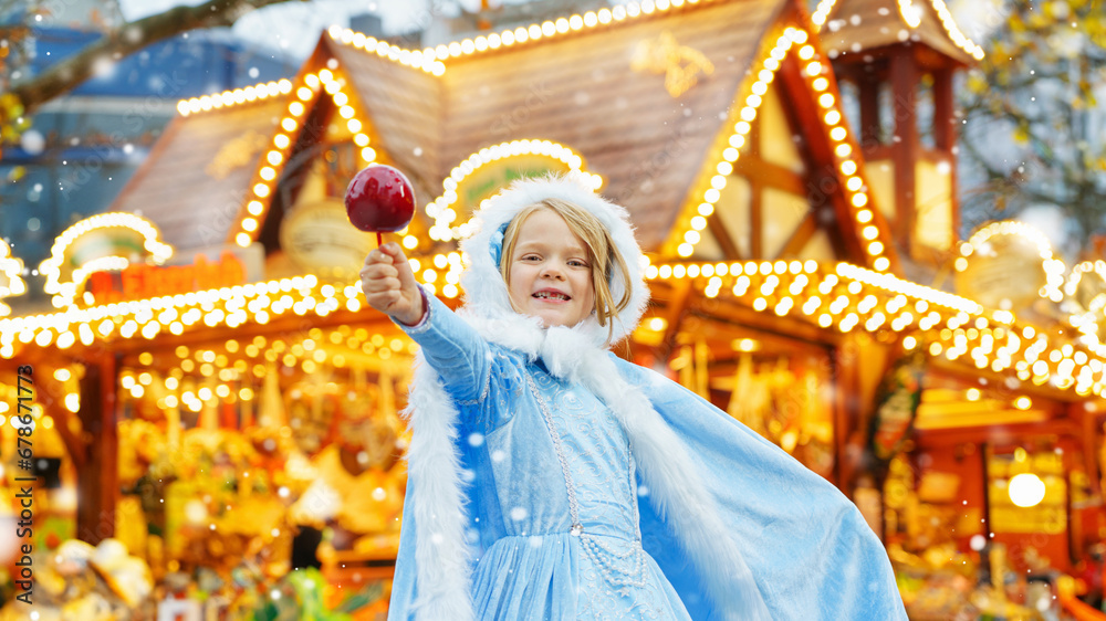 Fototapeta premium Little girl as snow white with candy sweet caramel apple from a sweets stand on Christmas market.