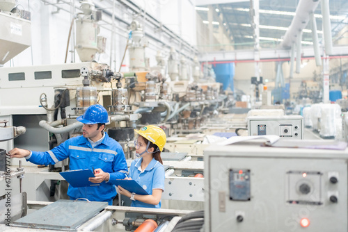American male engineer and Asian female manager working together Wear a uniform and safety helmet. Check the circuit boards of machines that are working in the company's plastics and steel factories.