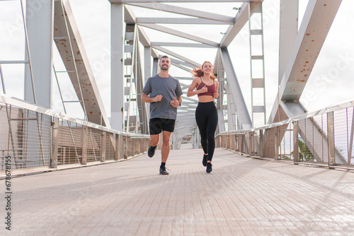Young adult friends doing a morning marathon in the morning outdoor. Man and woman jogging together with sport wear and smiling in a sunny day