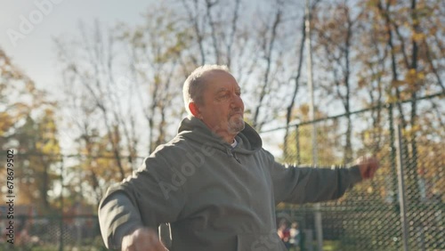 Elderly male pensioner in the park doing sports, doing exercises bending sideways photo