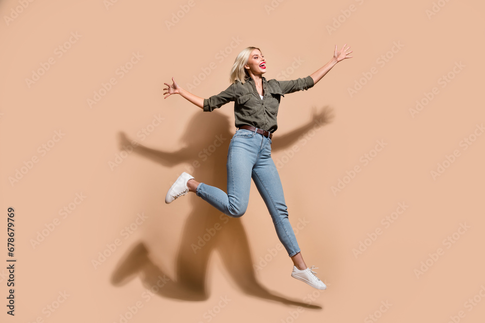 Full length photo of excited impressed woman dressed khaki shirt jumping high isolated beige color background Full length photo of excited impressed woman dressed khaki shirt jumping high isolated beige color background