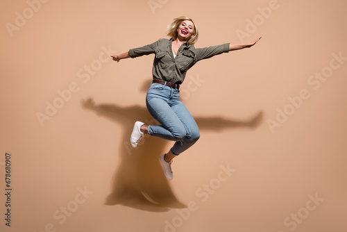 Full length photo of excited shiny lady wear khaki shirt jumping high isolated beige color background © deagreez