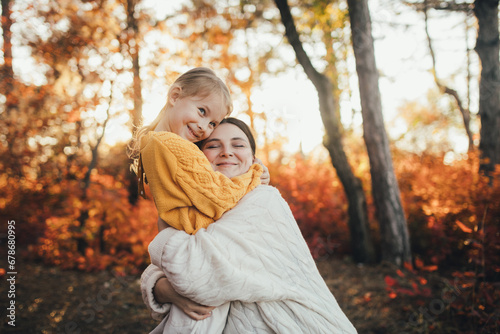 Young mother and her daughter walking together in a beautiful autumn forest.