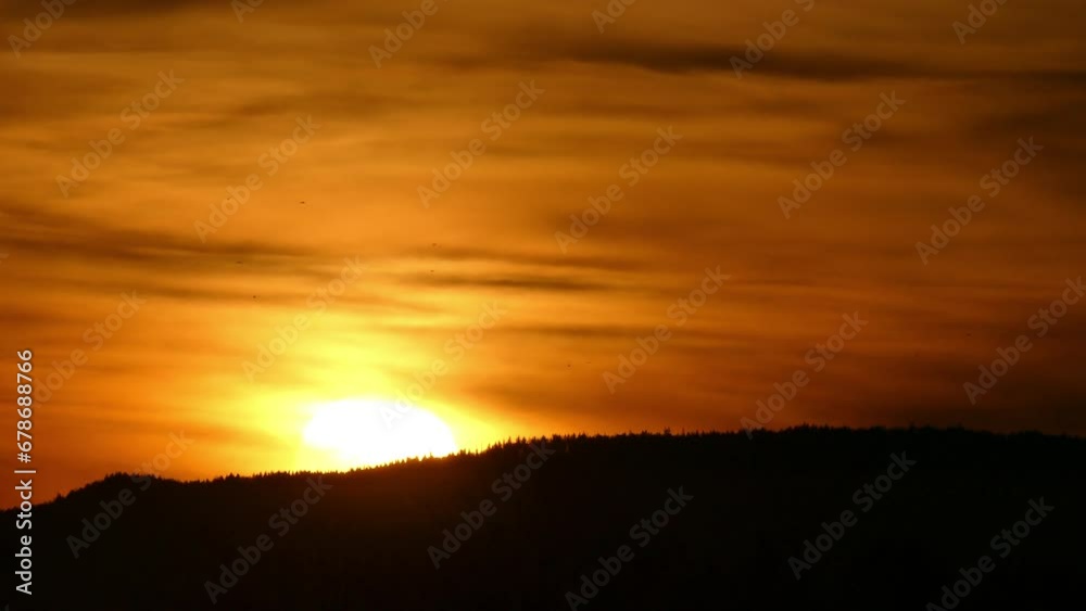 Sky with orange clouds, yellow sunrise, dark horizon of forests in mountains and birds in flight during rising sun in autumn morning - slow motion.