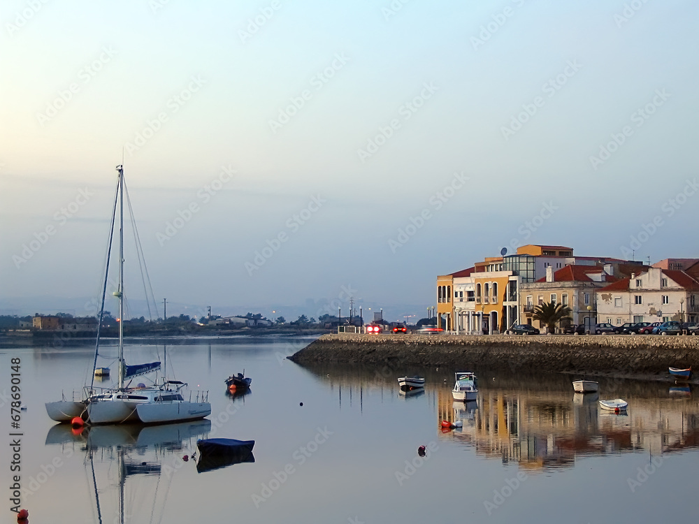 Seixal City and Seixal Bay view with small boats and a sailing trimaran at twilight, nightfall, dusk or evening. Setubal, Portugal