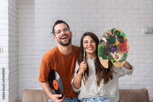 Young creative couple, artists musician and painter holding LP and colors palette with painting brush. Home of artwork