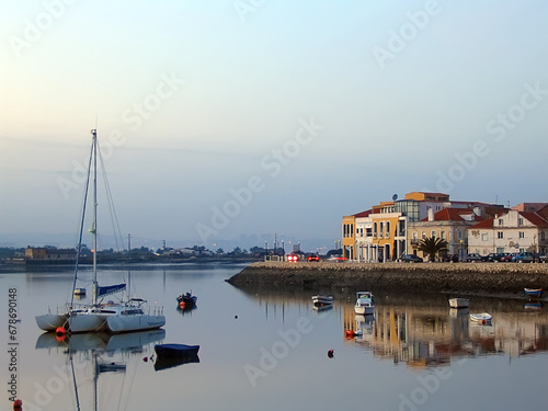 Seixal City and Seixal Bay view with small boats and a sailing trimaran at twilight, nightfall, dusk or evening. Setubal, Portugal
