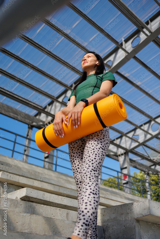 Fototapeta premium Fit and Fabulous: Young Woman Unfolding Mat in Stadium