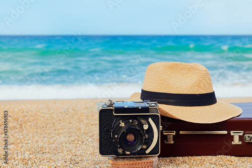 holiday at sea. a beige hat lies on a brown suitcase, the camera lies on the sand, waves in the background. summer vacation concept