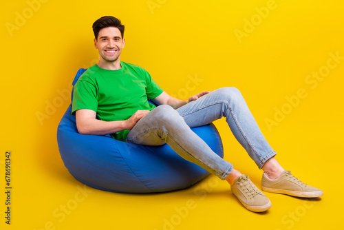 Full size photo of good mood guy wear stylish t-shirt denim pants sit on bean bag on coffee break isolated on yellow color background © deagreez