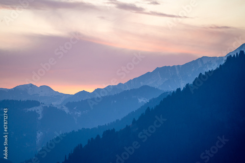 Pink blue hues of himalaya mountains fading off into fog showing the serene view from Manali Kullu vacation destination for winters and summers