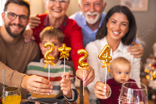 Family holding balloons shaped as numbers 2024 while having Christmas dinner at home