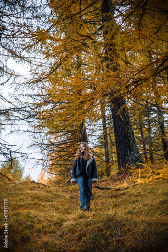 Young girl walking through forest in autumn colors of yellow and orange. Meran, South Tirol, Italy