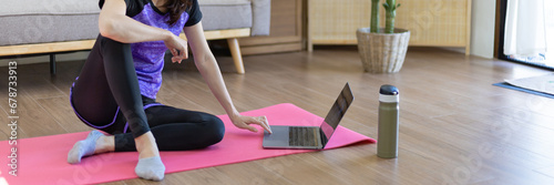 Woman looking at yoga teacher on laptop and doing light exercise in the living room at home, Watch live teaching or VDO on laptop, Dumbbells and a protein shake or bottle of water, Healthy exercise.