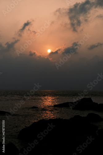 Natural sunset over the sea in warm colors with an endless horizon and reflection of the sun. Romantic view of the sunset and shadows of the rocks along the beach