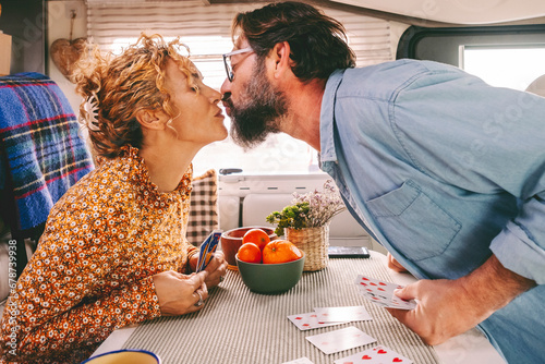 Couple enjoy leisure time playing cards and kissing with love inside a camper van. Travel and holiday vacation concept. Van life for travel people. Young adult man and woman in relationship indoor #678739938