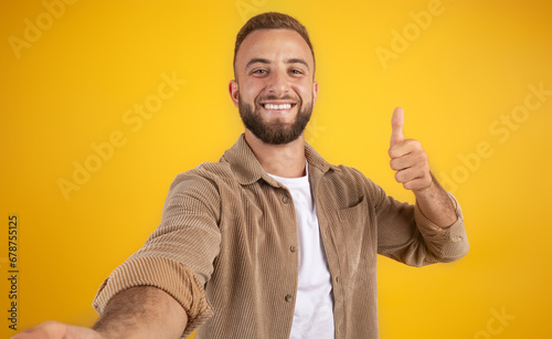 Happy millennial european guy with beard in casual make thumb up hand sign, make selfie