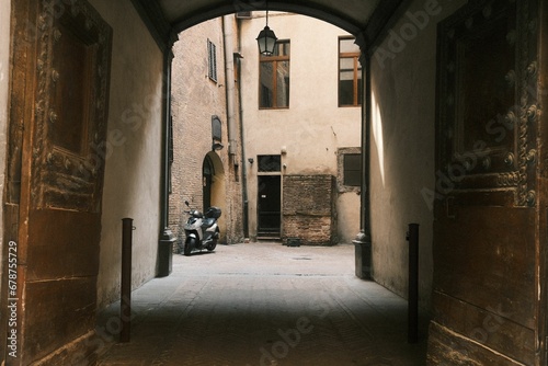 Archway in Siena Centro with a big wooden door exit to a small yard with a parked gray moped