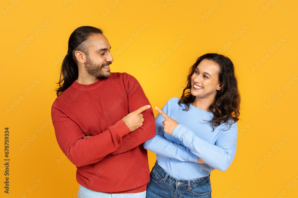 Positive millennial couple pointing at each other and smiling