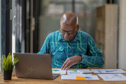 Black senior man in casual clothes carefully reviews project work and performance for continuous growth and development.