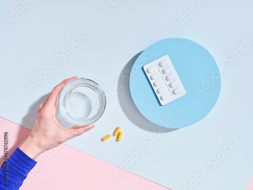 Flat lay creative composition with food supplement pills, glass of water and female hand on colorful background