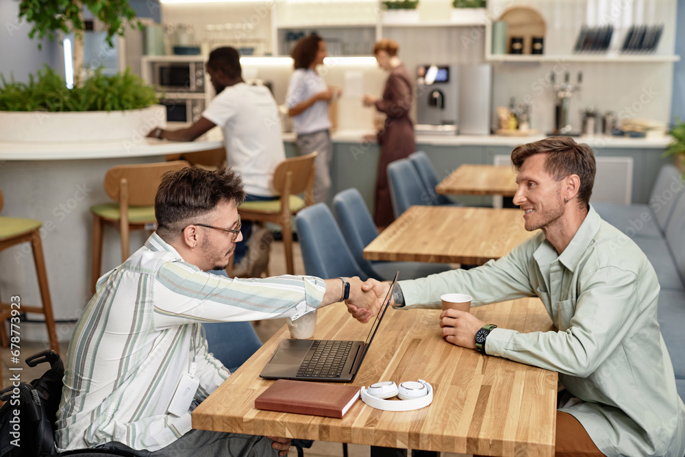 Colleagues shaking hands while sitting at table in coffee shop and having meeting