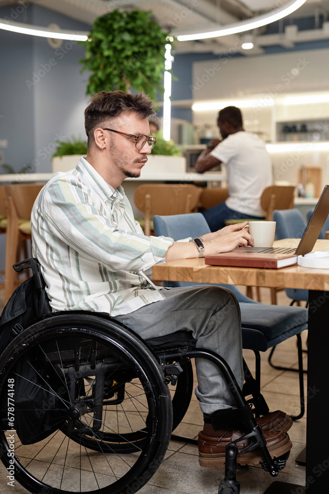 Vertical image of man with disability sitting in coffee shop and working online on laptop