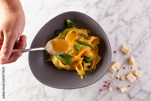 hand adding tasty sauce to pasta on plate on marble table photo