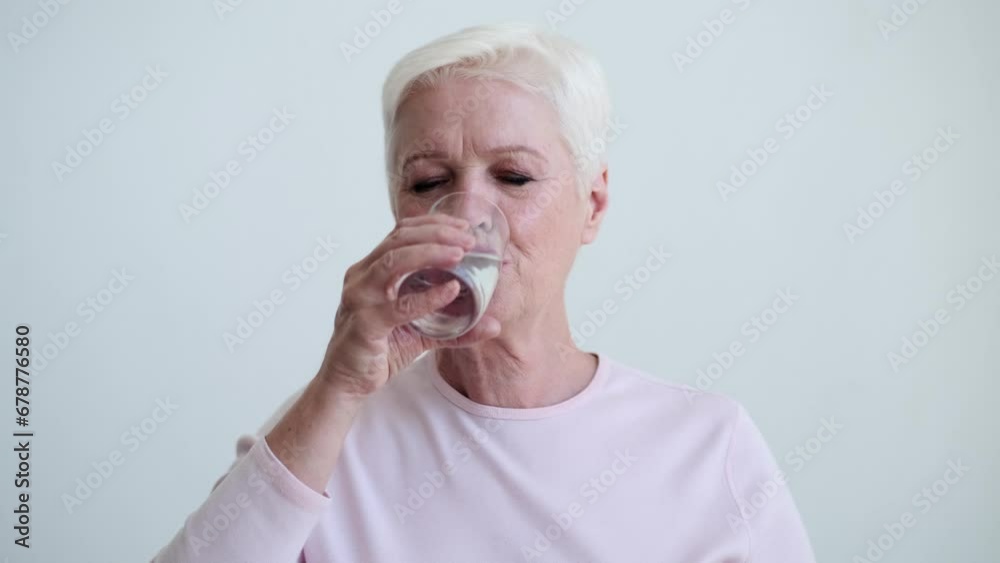 Mature Caucasian woman delicately sips water from a glass. Expression is serene, reflecting the quiet satisfaction that comes from taking care of herself. The gentle curve of the glass meets lips. Mature Caucasian woman delicately sips water from a glass. Expression is serene, reflecting the quiet satisfaction that comes from taking care of herself. The gentle curve of the glass meets lips.