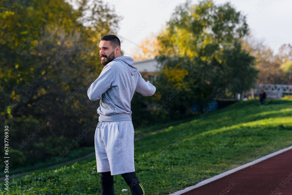 Young fit man warming up on a jogging track, getting ready for a jog on a sunny day