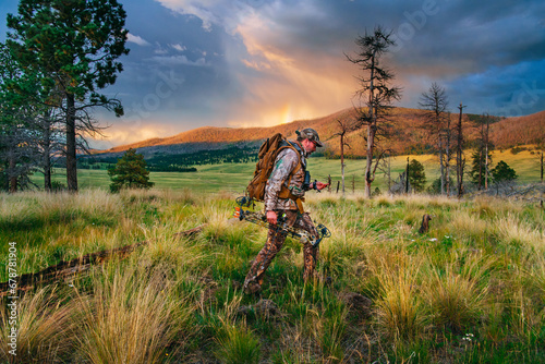 A man in full camouflage hikes while bowhunting in the backcountry of Valles Caldera National Preserve, New Mexico, with thunderclouds in the distance photo
