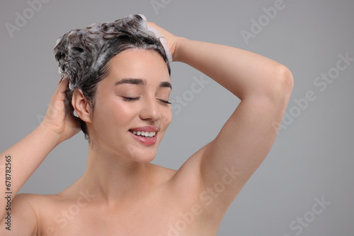 Beautiful happy woman washing hair on grey background